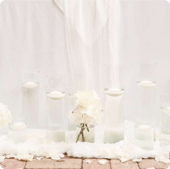 vizi gyertyák magas üvegekben fehér szirmok között az asztalok lábánál